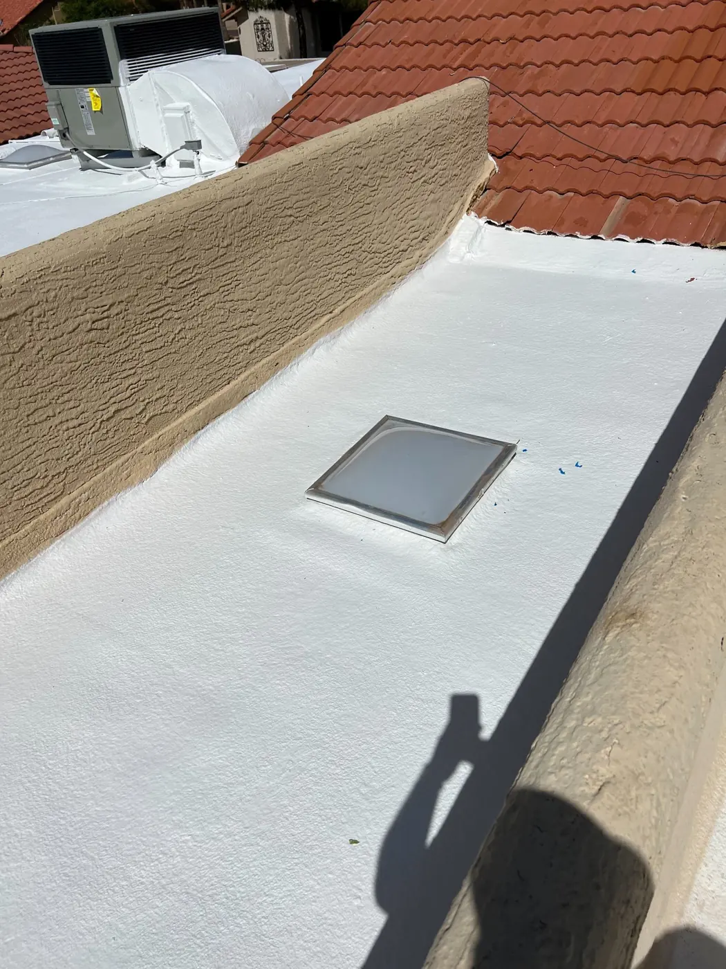 Coated flat roof with a skylight behind a stucco parapet