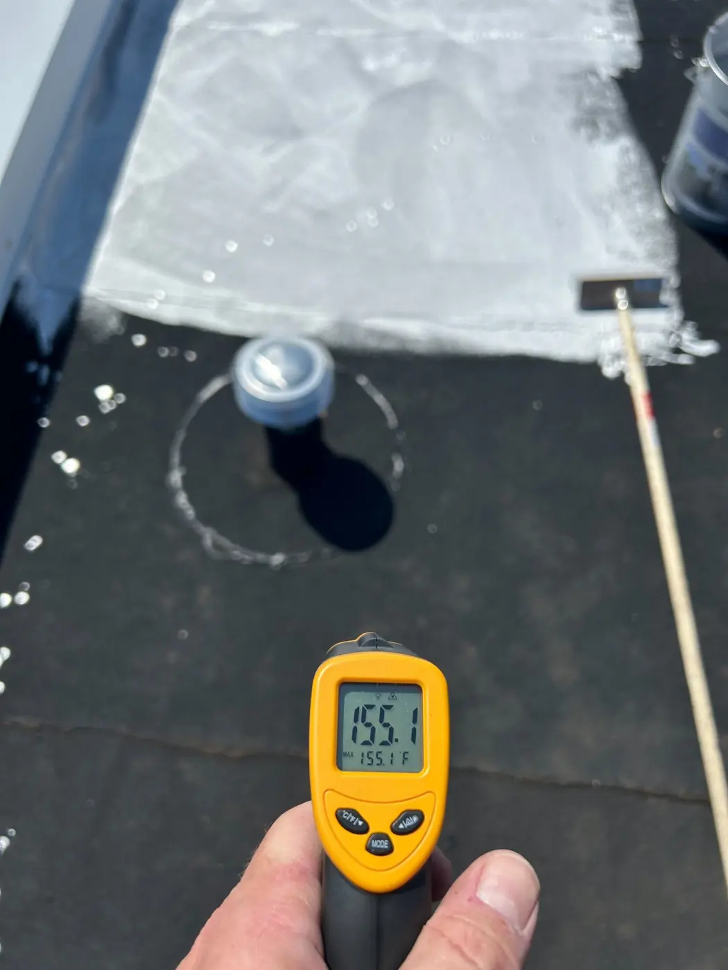 Infrared thermometer reading 155.1°F on a bare black roof