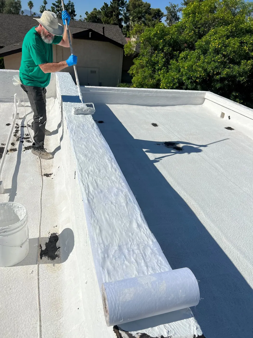 Roofer rolling coating along a parapet wall